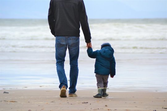 assurance vie enfant-homme qui tient la main de son enfant en bord de mer